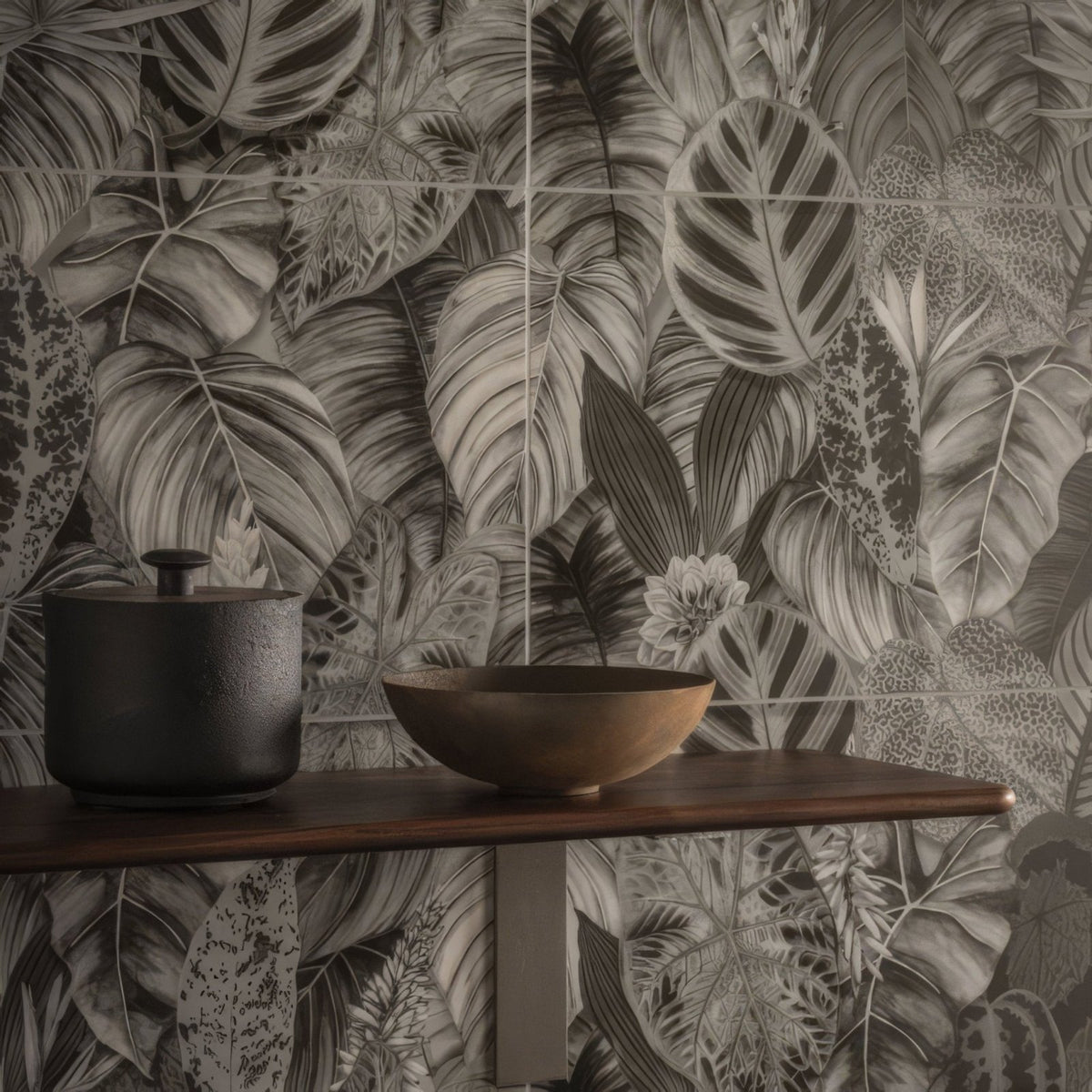 Dark matte-finished ceramic pot with small black lid beside wooden bowl on shelf in tropical oasis monochrome tile