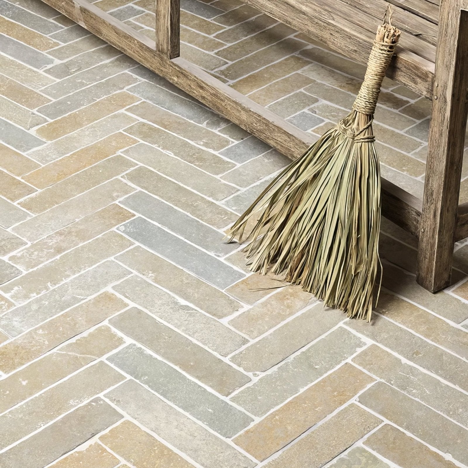 A rustic straw broom with natural fiber handle resting against a wooden bench next to trusloe limestone seasoned finish parquet