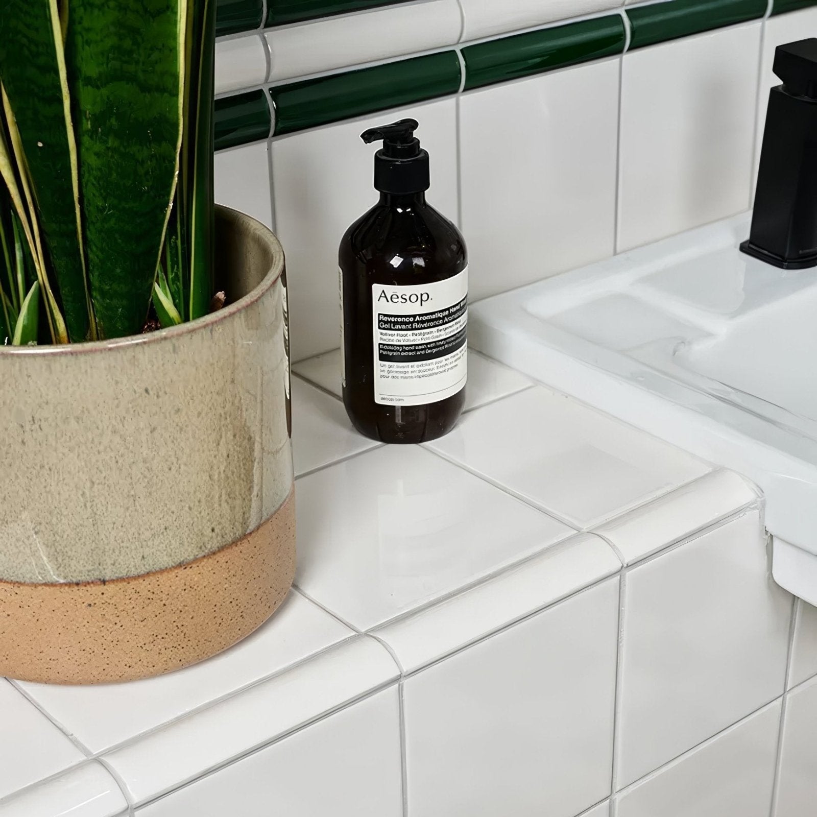 Aesop sleek dark amber glass bottle with black pump and white label placed on Victorian Style wall ceramic white square