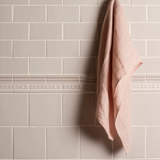A soft pink textured linen towel hanging against a waveney field tile wall