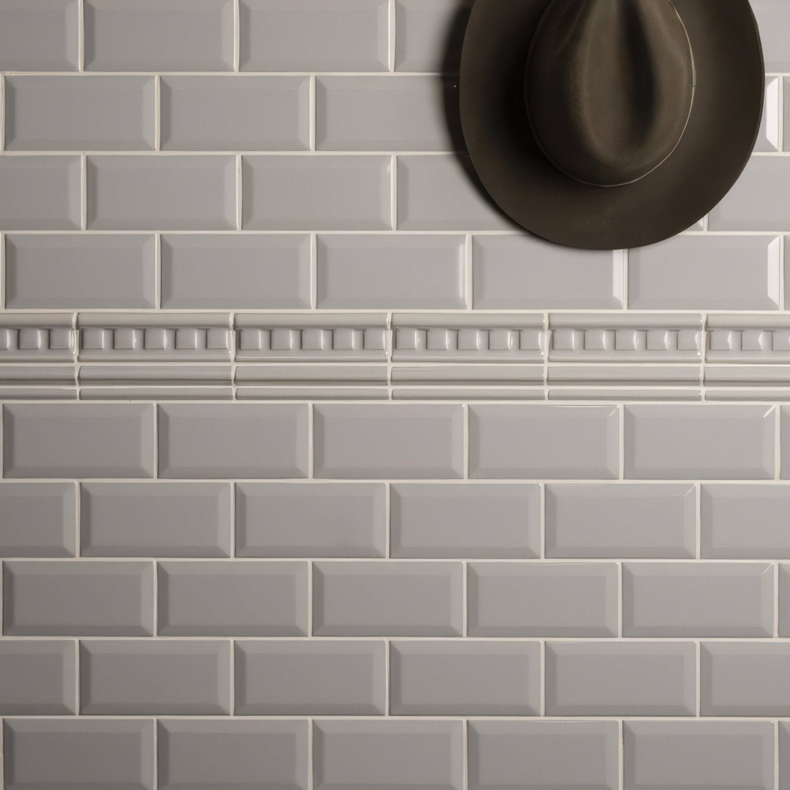 A dark brown fedora hat resting against light gray subway tiles in a product setting titled westminster grey dentil moulding