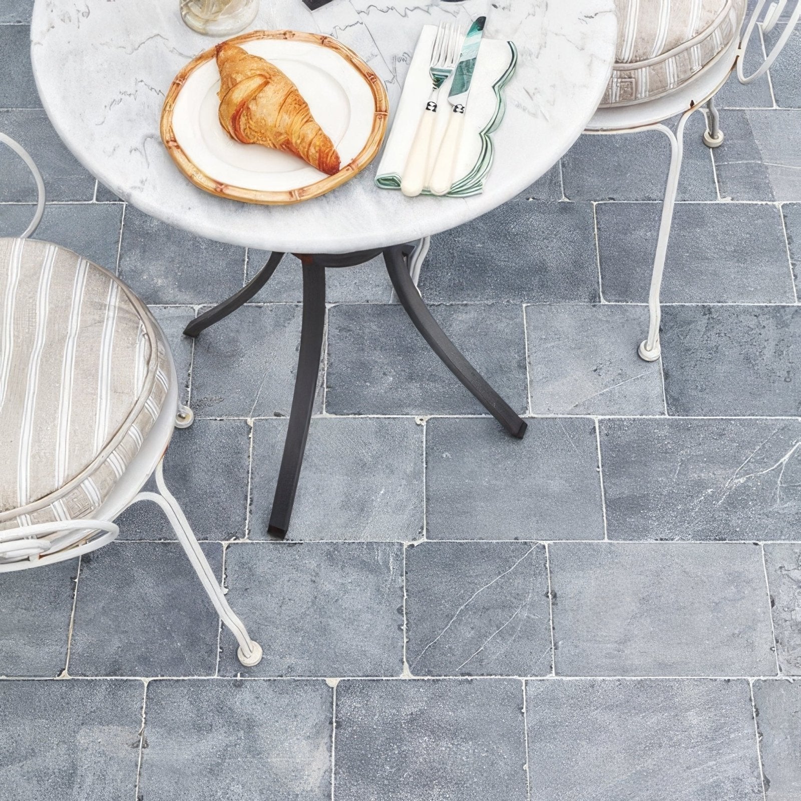Golden-brown croissant on a white plate with bamboo-patterned rim on wexford limestone cobble tumbled finish surface