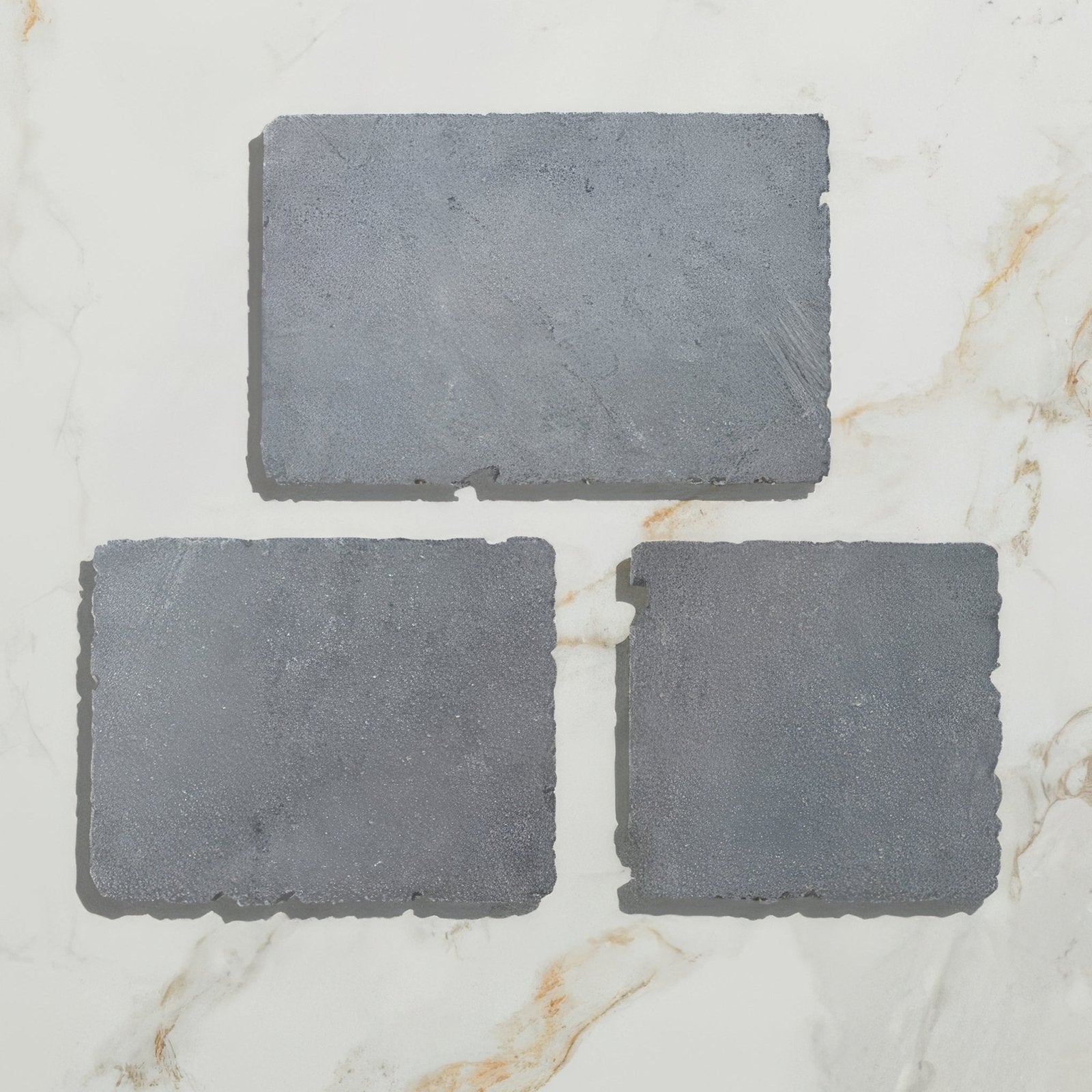 Three rectangular gray slate tiles with rough edges and textured surface in wexford limestone cobble tumbled finish