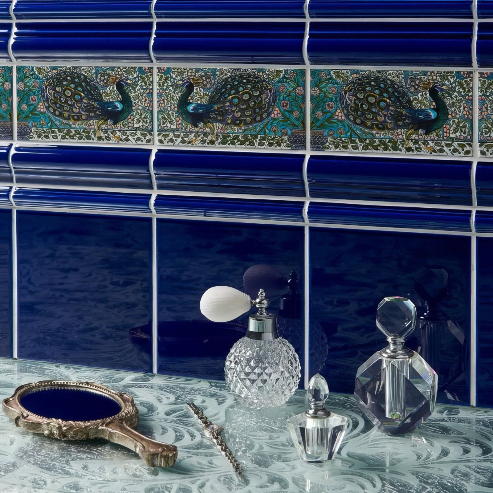 Crystal perfume bottle with faceted geometric design and silver-toned cap on william de morgan peacock border tile set