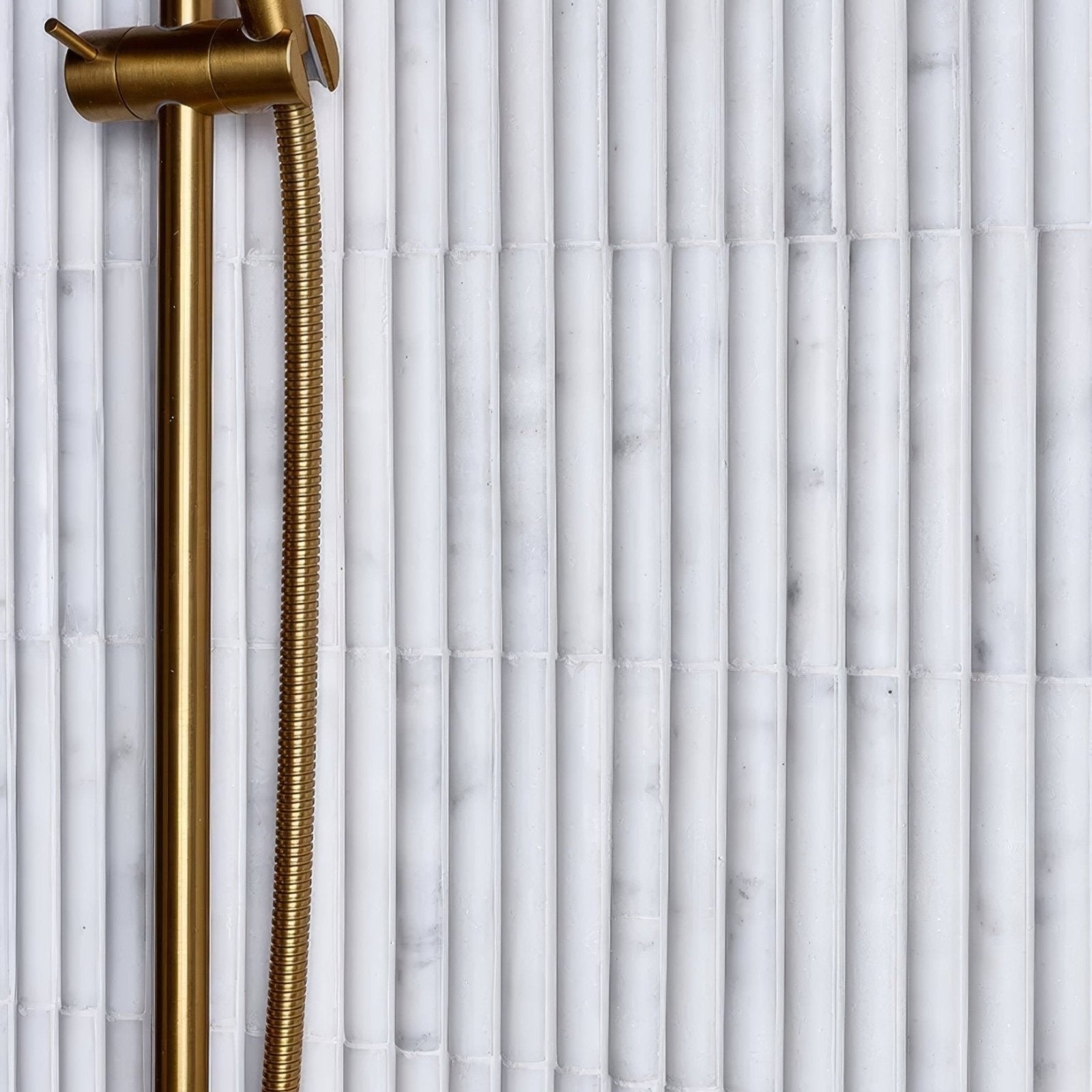 Gold-toned flexible corrugated shower hose attached to a brass fixture for the zen marble reed mosaic design