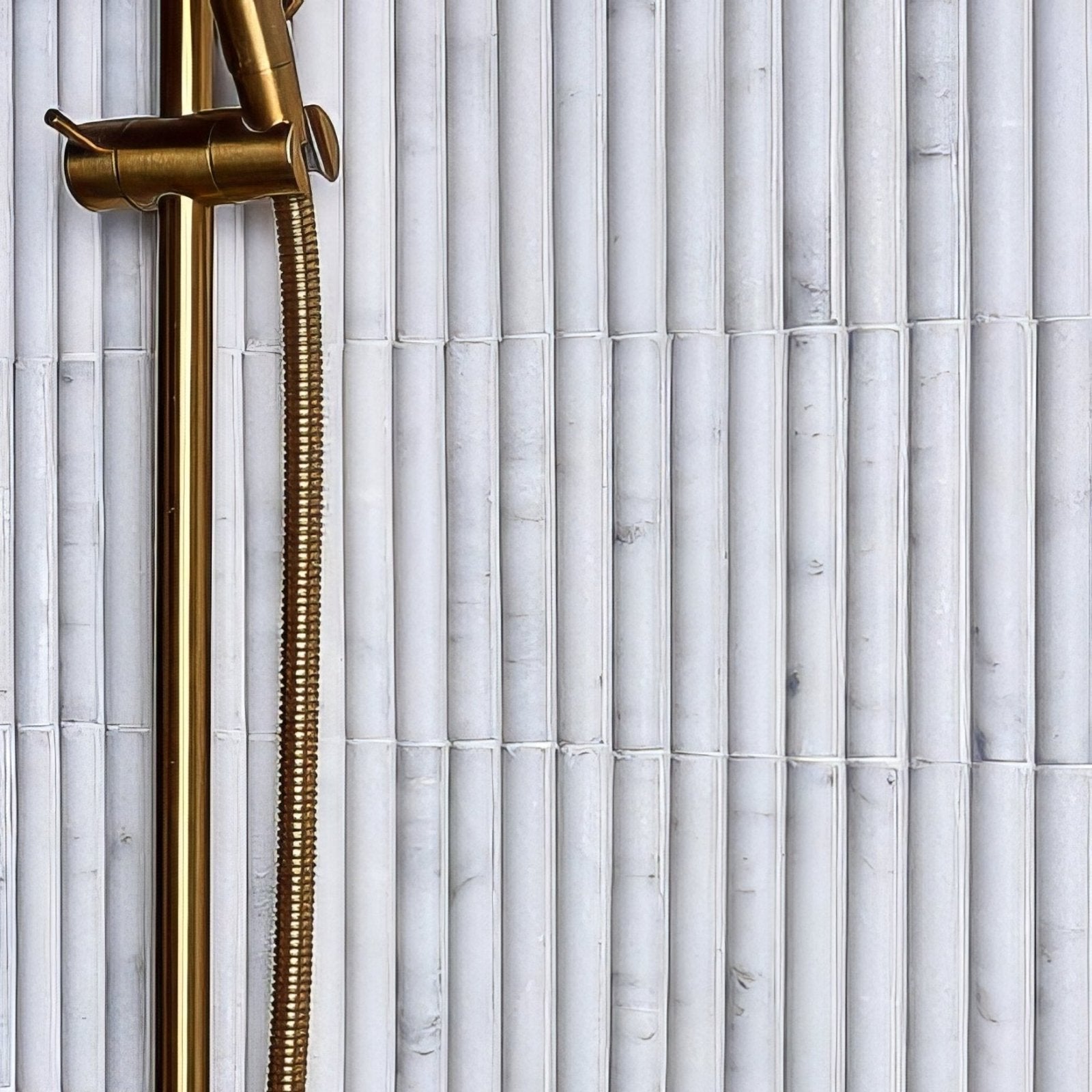 Gold-toned showerhead with sleek modern design and brass hose mounted on white marble-veined zen marble reed mosaic tiles