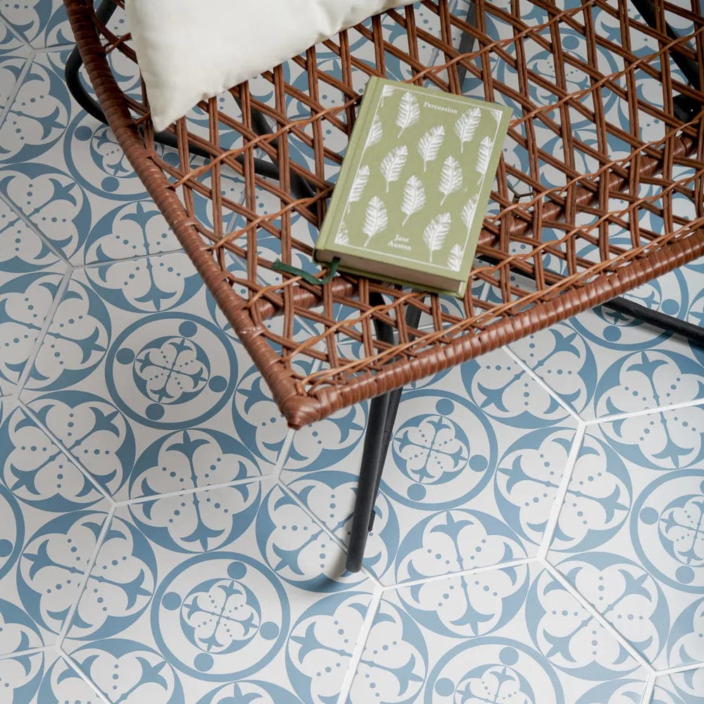 A green book with white feather illustrations rests on a brown wicker chair in the carnaby hexagon sky product line