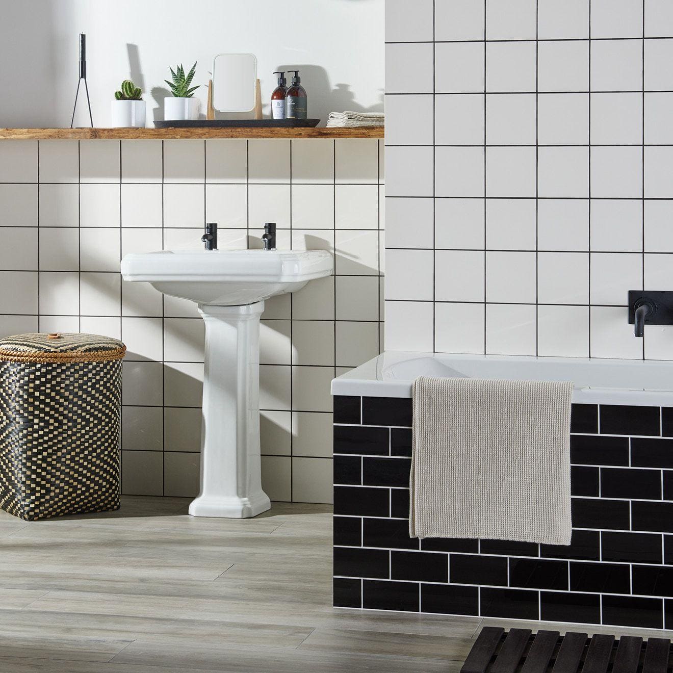 White ceramic pedestal sink with black faucet fixtures installed against daisy satin field tile wall