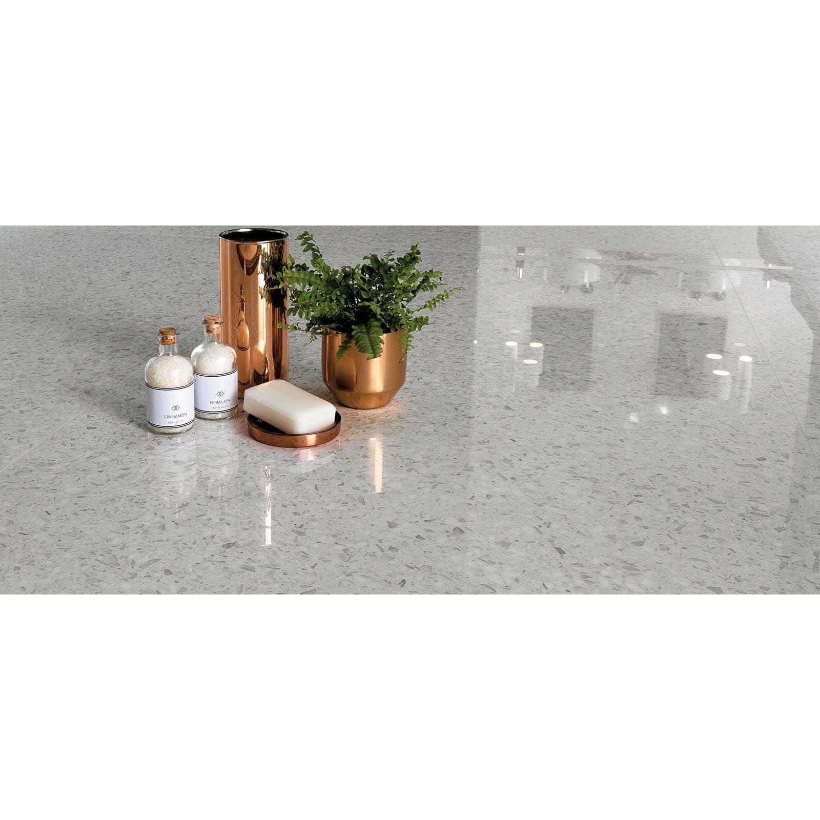 Rose gold cylindrical soap dispenser with sleek reflective surface and minimalist design on gemstones terrazzo white matt tile