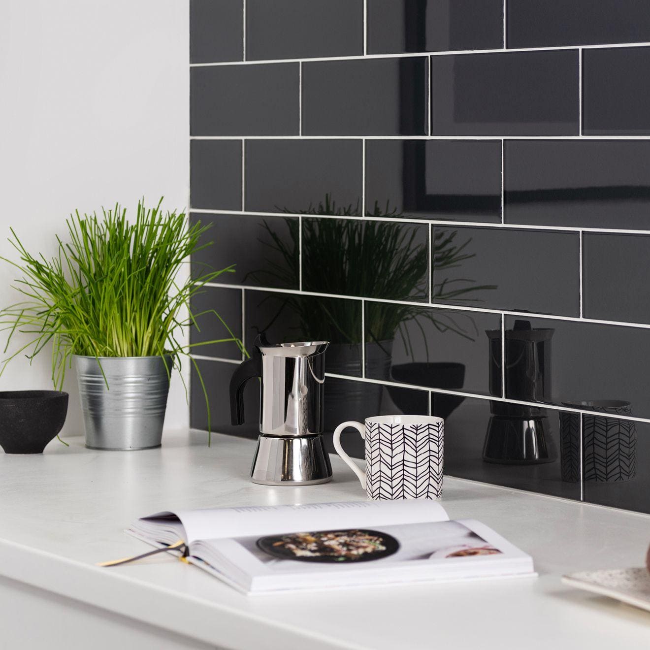 A sleek stainless steel moka pot with polished finish and black handle on countertop from hermes metallica collection