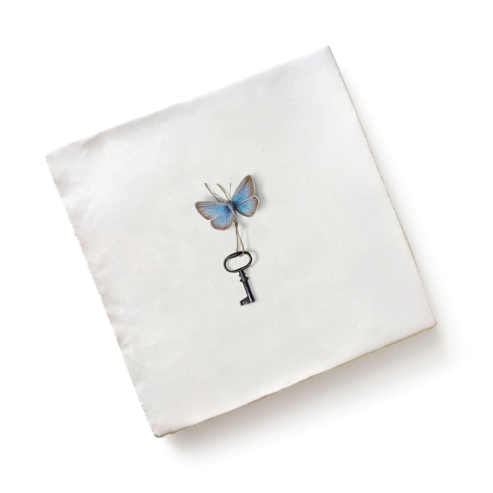 A delicate blue and silver-toned ceramic butterfly perched on a vintage-style black key by Michael Angove
