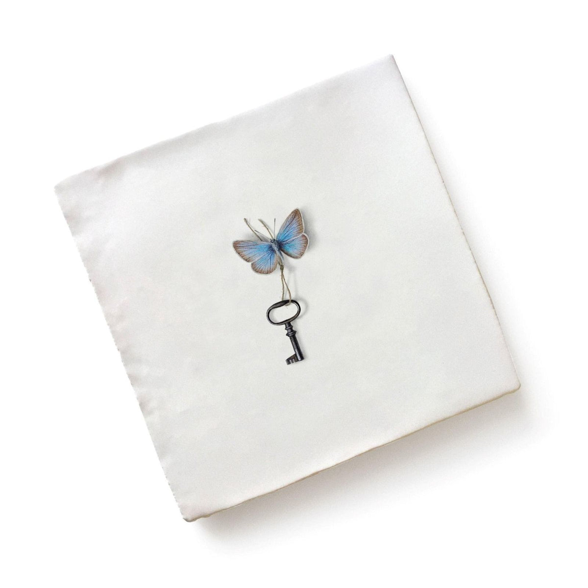 A delicate blue and silver-toned ceramic butterfly perched on a vintage-style black key by Michael Angove