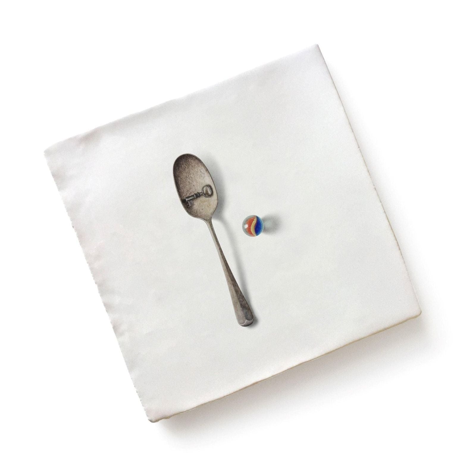 Menagerie ceramic silver spoon with key design on bowl resting beside multicolored glass marble by michael angove