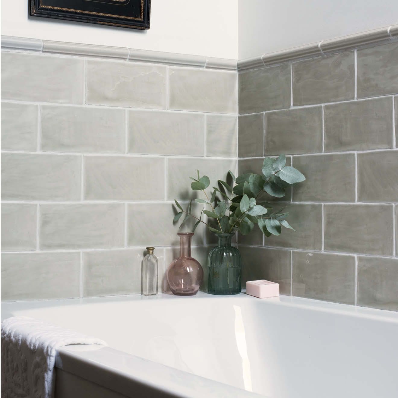 A pair of glass vases in dusty rose and deep teal sit on the edge of a white bathtub with mere ogee moulding