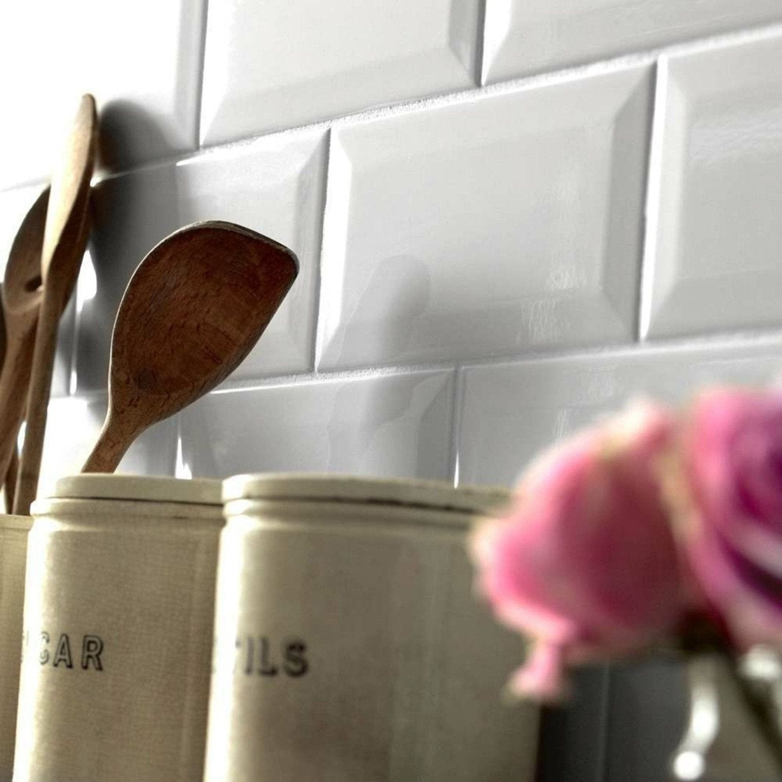 A rustic wooden spoon with a smooth finish resting in a cream-colored ceramic metro blanco gloss canister