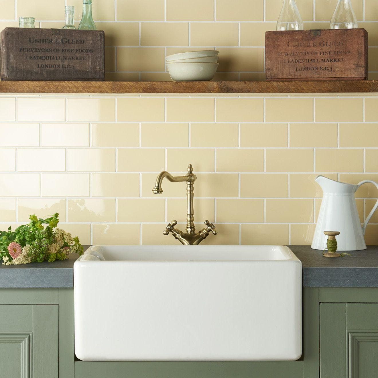 White ceramic farmhouse sink with brass faucet featuring regency cream half tile backsplash in kitchen setting
