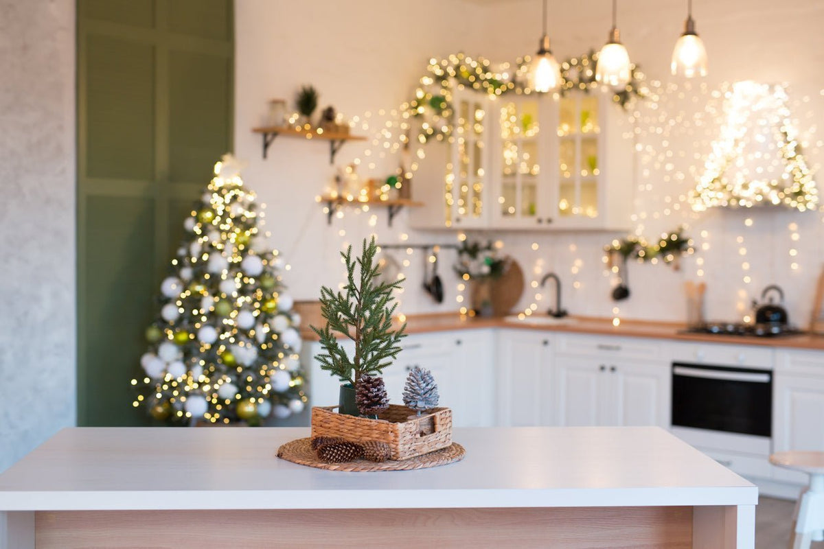 A small green pine tree in a woven wicker basket with decorative pinecones and snow-covered cones for kitchen wall decor.