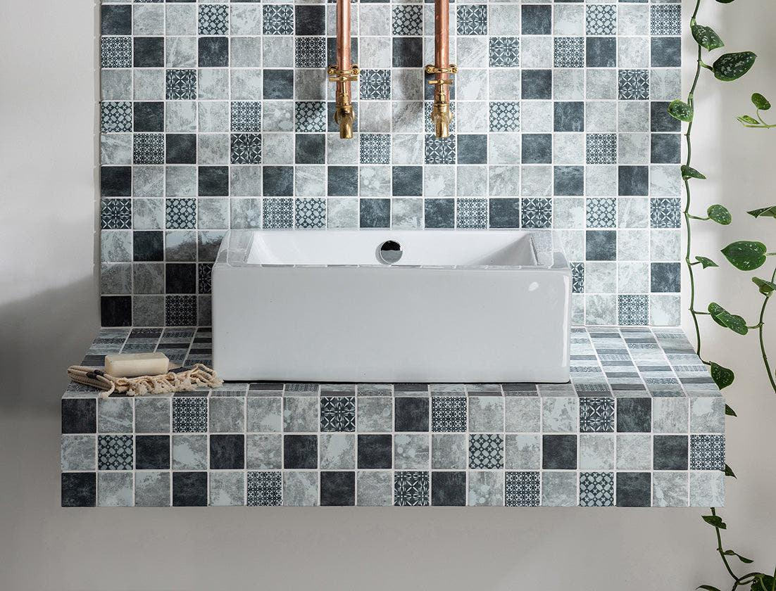 White rectangular ceramic sink with central drain set into floating vanity with gray and black mosaic tiles for luxury bathroom