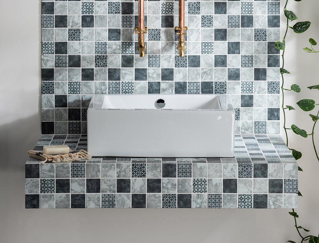 White rectangular ceramic sink with central drain set into floating vanity with gray and black mosaic tiles for luxury bathroom