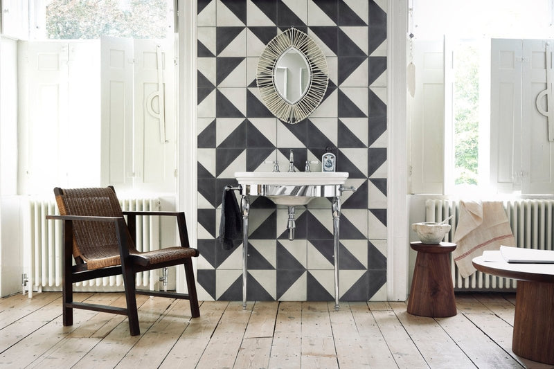 White ceramic sink with chrome legs and polished metallic faucet mounted on black and white geometric tiled wall