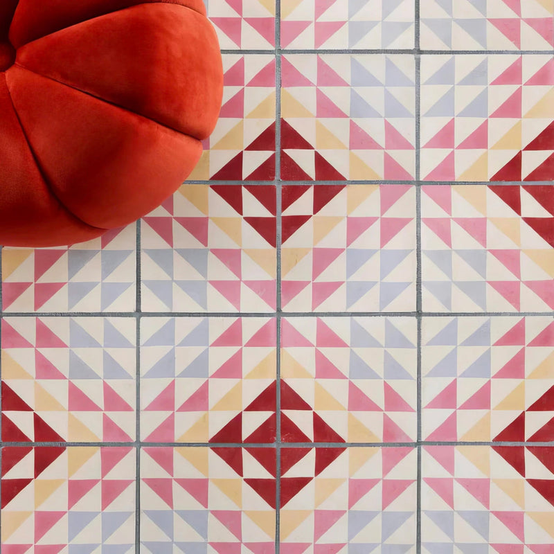 A plush red velvet armchair with a rounded segmented design sits against geometrically patterned tile walls