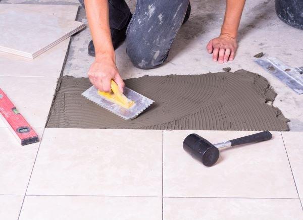 A yellow-handled notched metal trowel used for spreading tile adhesive in removing ceramic and porcelain floor tiles