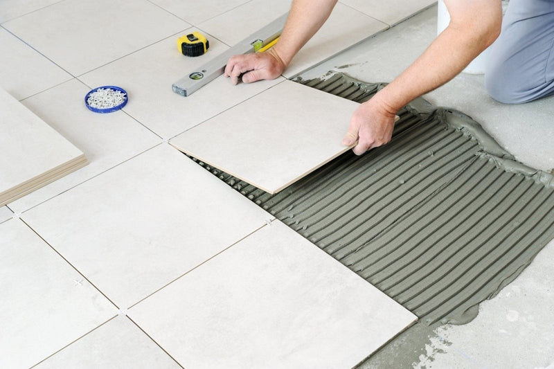 Light gray rectangular ceramic floor tile being installed with adhesive in a how to remove ceramic floor tiles article