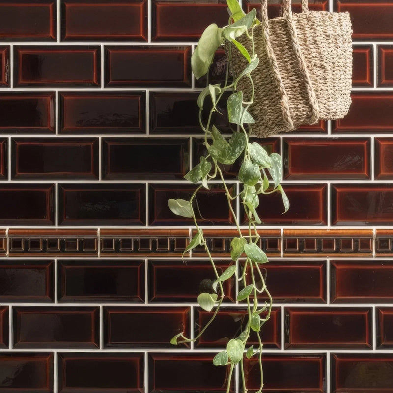 A woven wicker hanging basket in natural beige color suspended against glossy dark brown 20 x 10cm wall tiles
