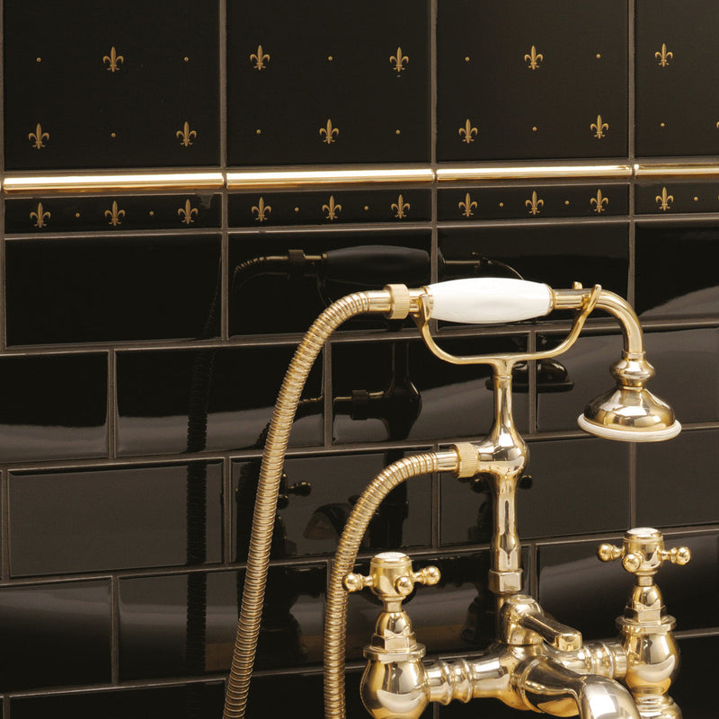 Brass bathtub faucet with white ceramic handle and spout set against black tiled wall from artworks fleur de lis 2-tile set