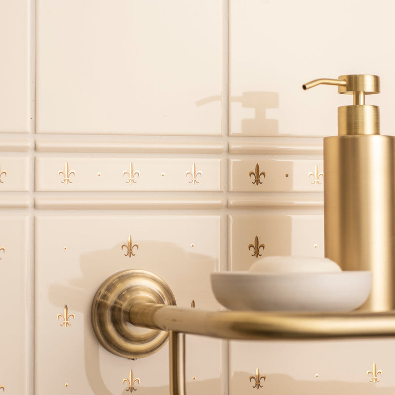 Gold-toned soap dispenser with sleek cylindrical body and polished pump in artworks fleur de lis border collection