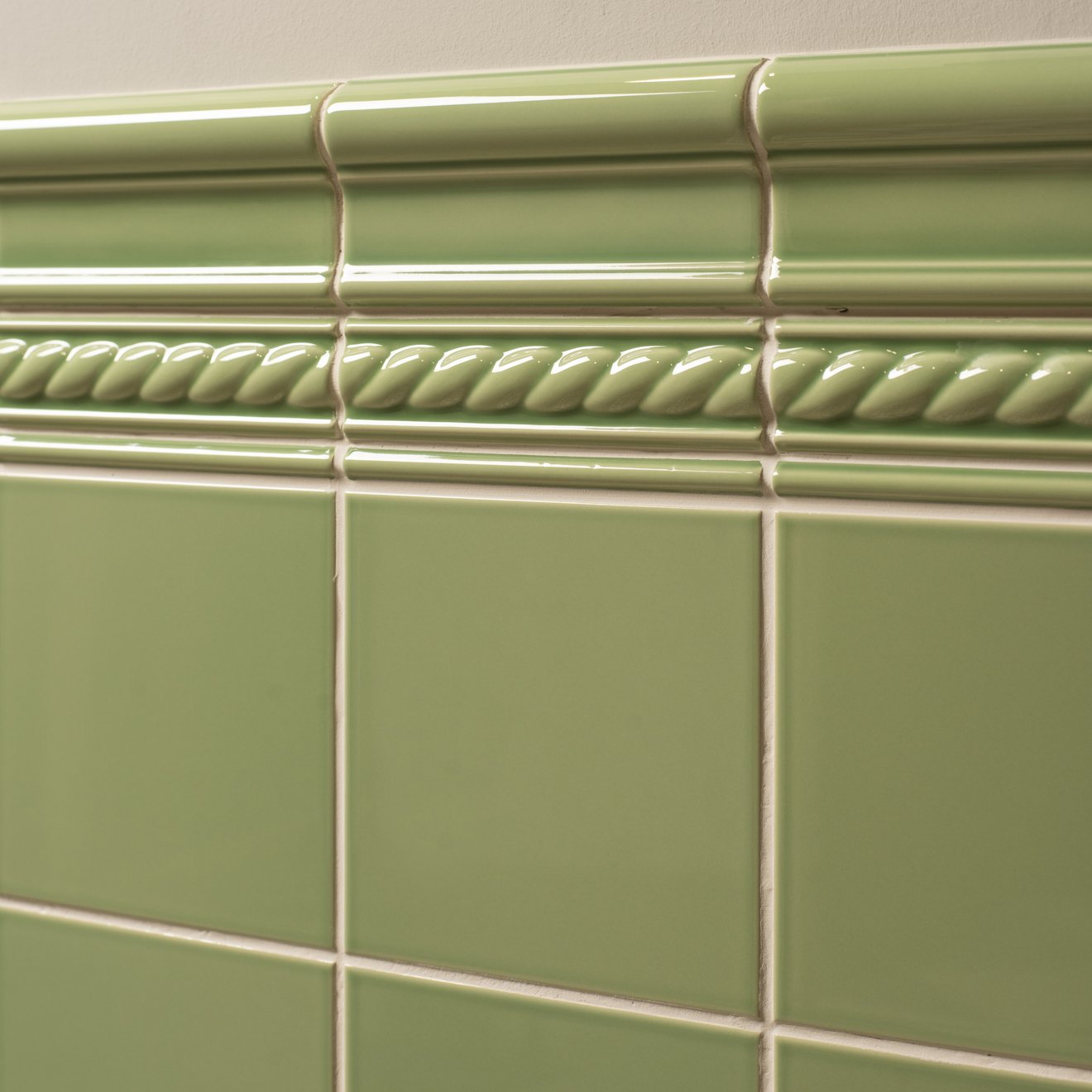 Light green ceramic tile with glossy finish and decorative rope-like molding above square tiles from artworks rope moulding collection.