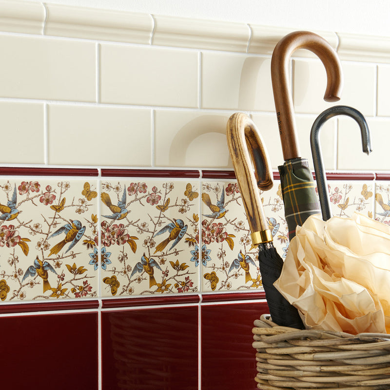 A decorative ceramic tile strip with birds butterflies and blossoms in soft blues golds and pinks on county white