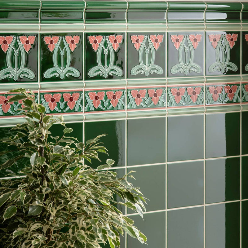 Deep green ceramic dauphine border tile with art nouveau pink and light teal floral patterns in decorative bands