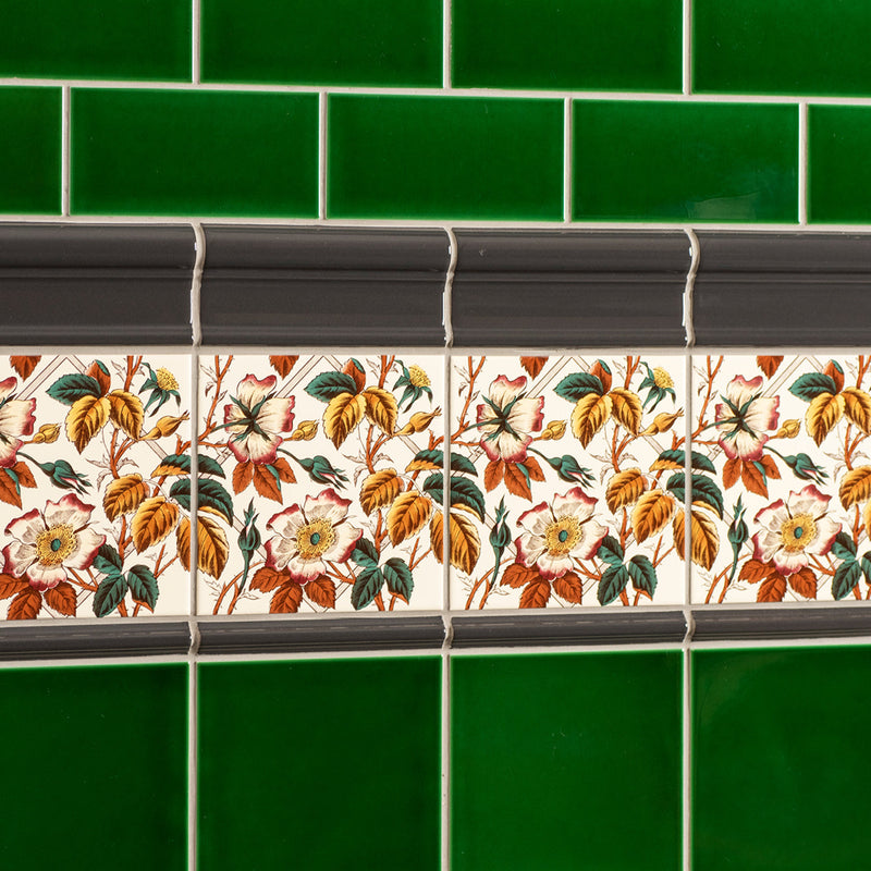 A decorative ceramic tile strip featuring pink and yellow roses with green leaves on an off-white county white background