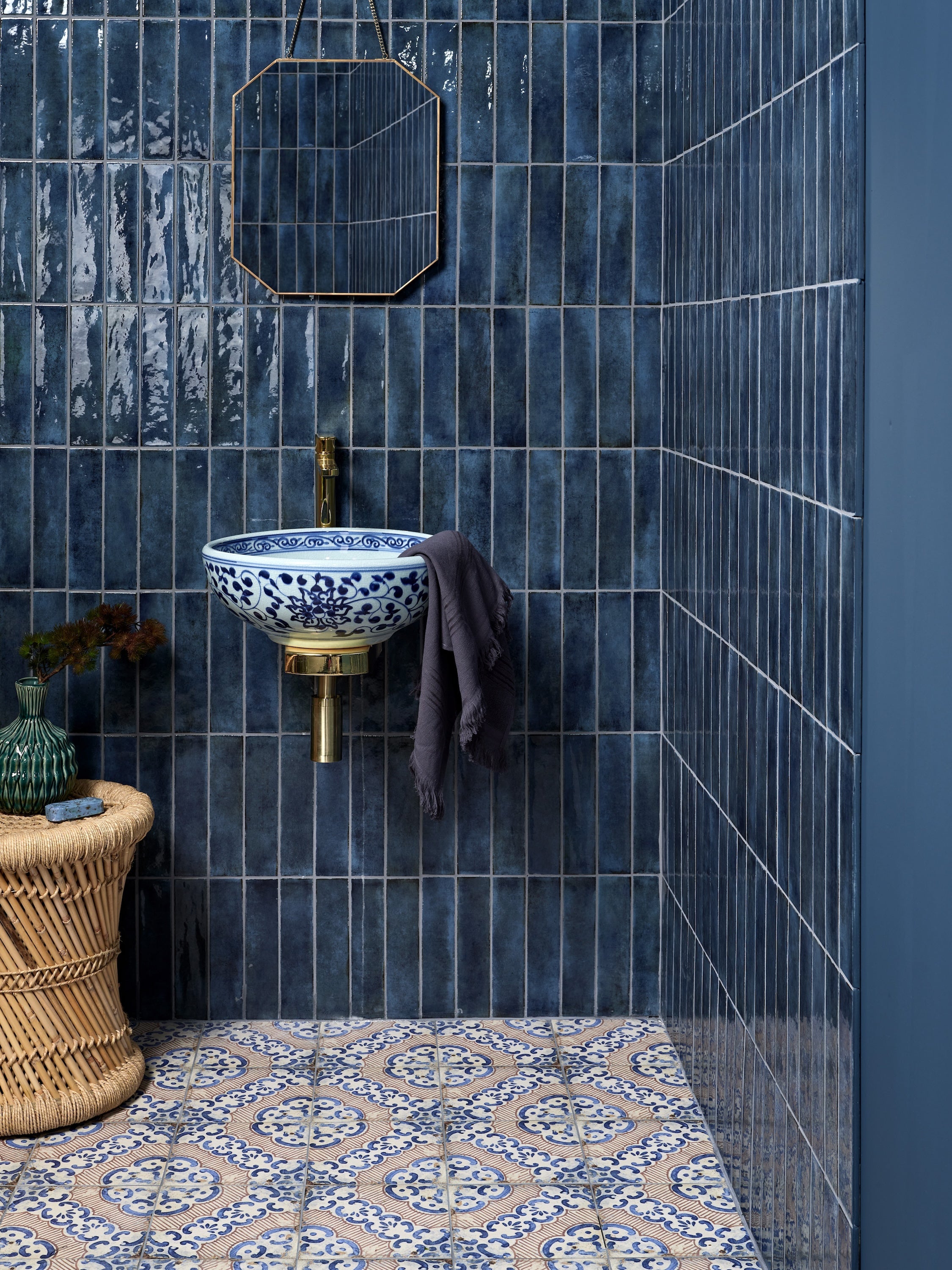 Blue and white porcelain sink with intricate floral patterns mounted on brass fixture against dark blue tiled walls