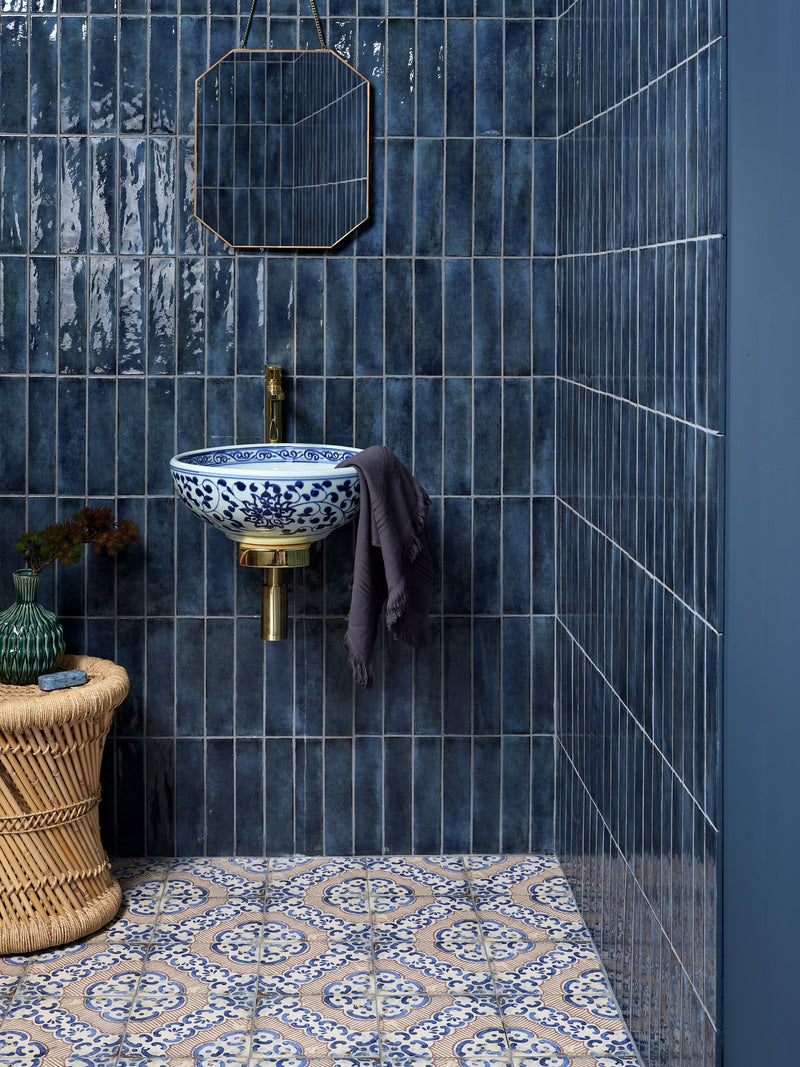 Blue and white porcelain sink with intricate floral patterns mounted on brass fixture against dark blue tiled walls