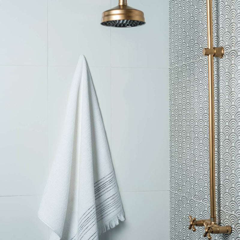 White towel with delicate black striped border and frayed edge hanging neatly in a modern bathroom setting