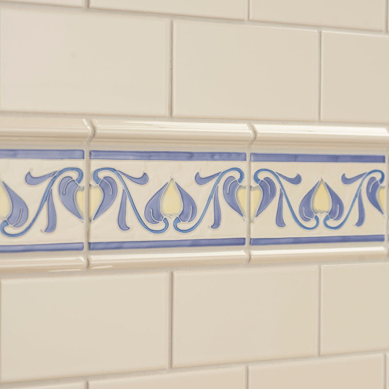 A decorative ceramic lilium tubelined border tile strip with blue and cream floral motifs on a white tiled wall