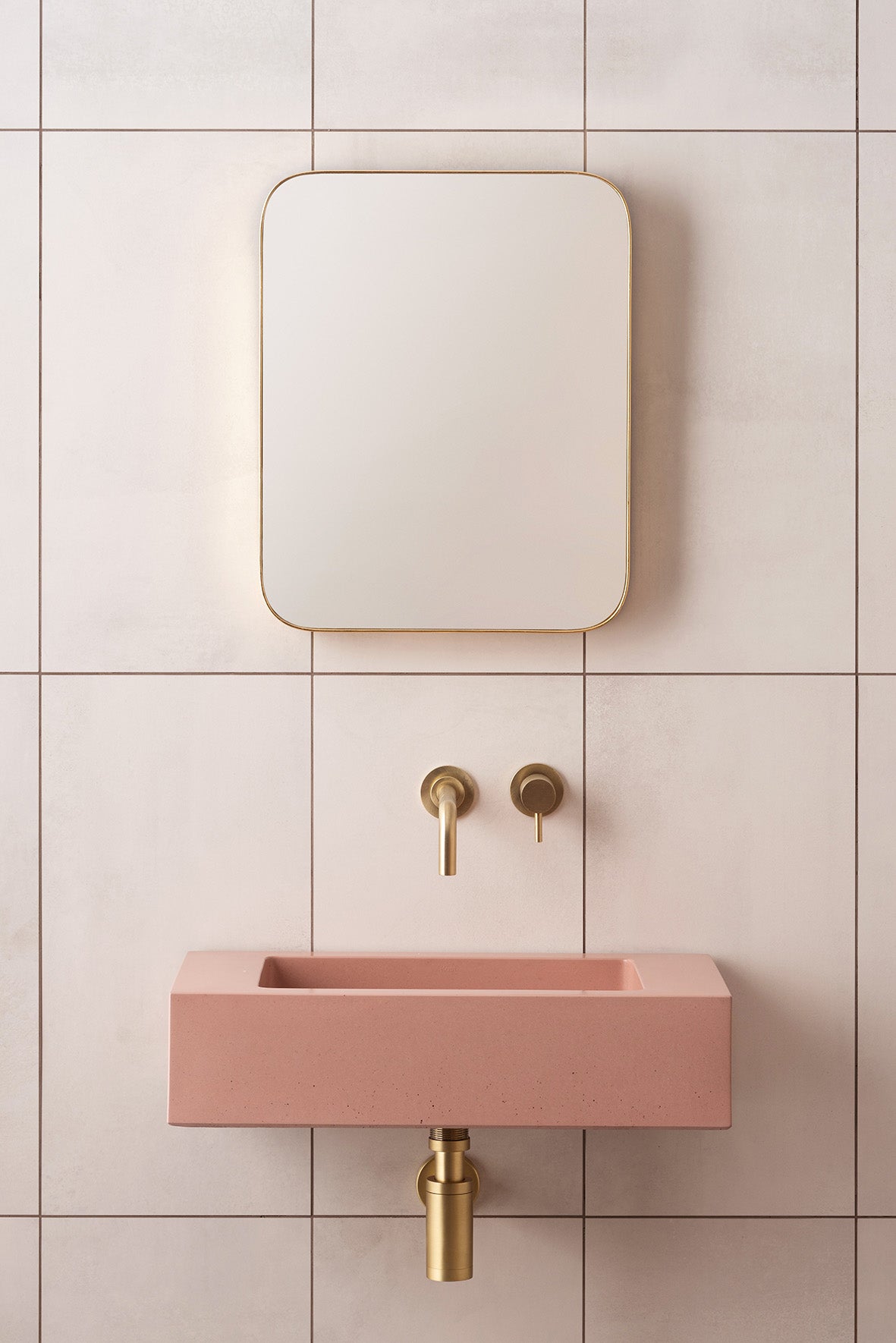 Pink rectangular concrete sink with gold-toned faucet and matching wall-mounted mirror in stylish bathroom tiles collection