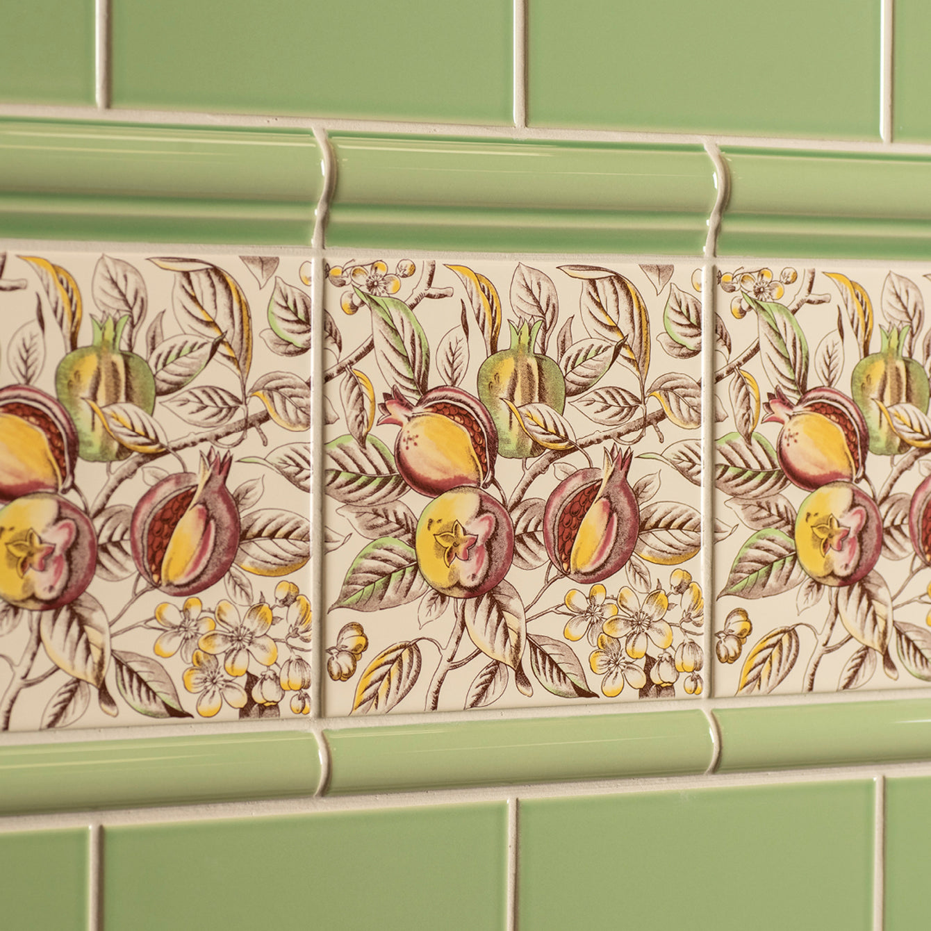 Beige ceramic pomegranate decorative tile with detailed botanical design and light green border from county white collection