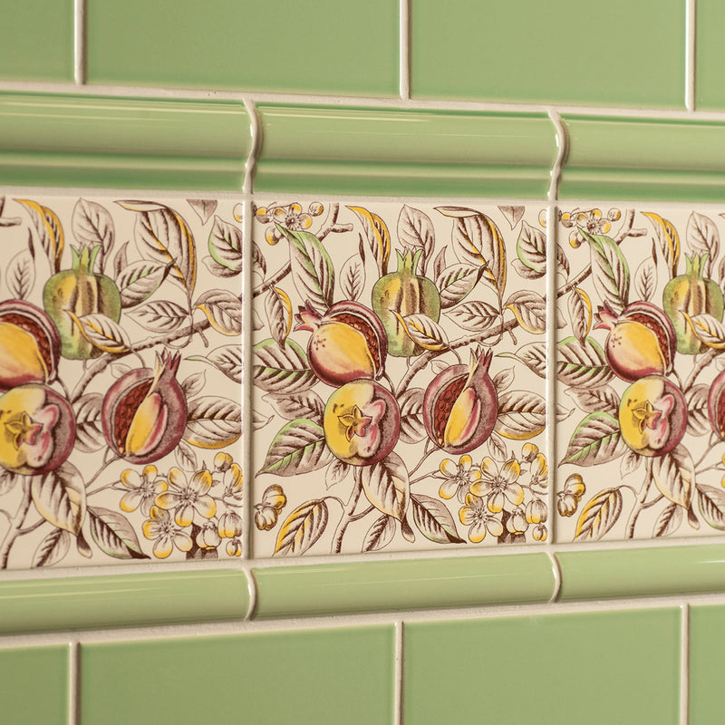 Beige ceramic pomegranate decorative tile with detailed botanical design and light green border from county white collection