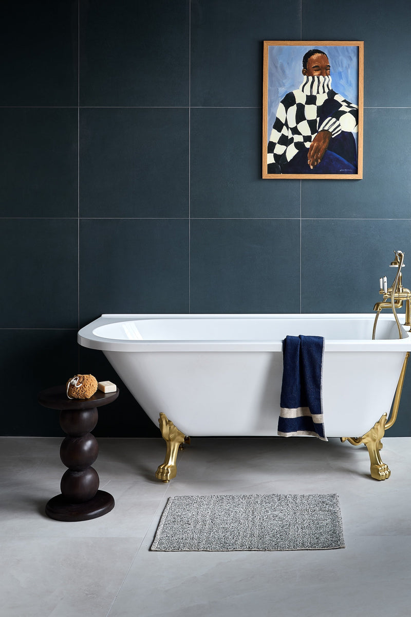 White clawfoot bathtub with gold-colored feet and brass faucet in stucco porcelain textured collection.
