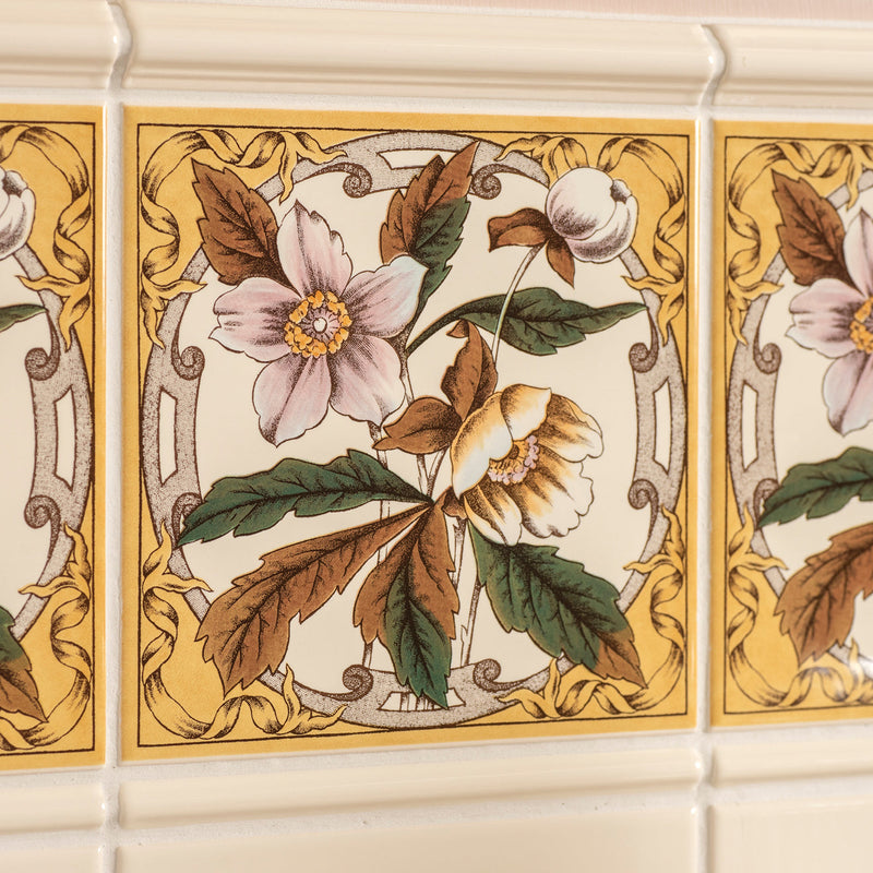 Beige ceramic windflower decorative tile on county white with ornate pink and cream floral design framed by gold scrollwork.