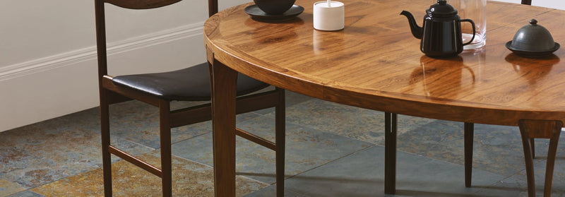 A polished medium-toned wooden oval dining table with dark metal legs and matching chair in ardosia natural slate flooring collection.