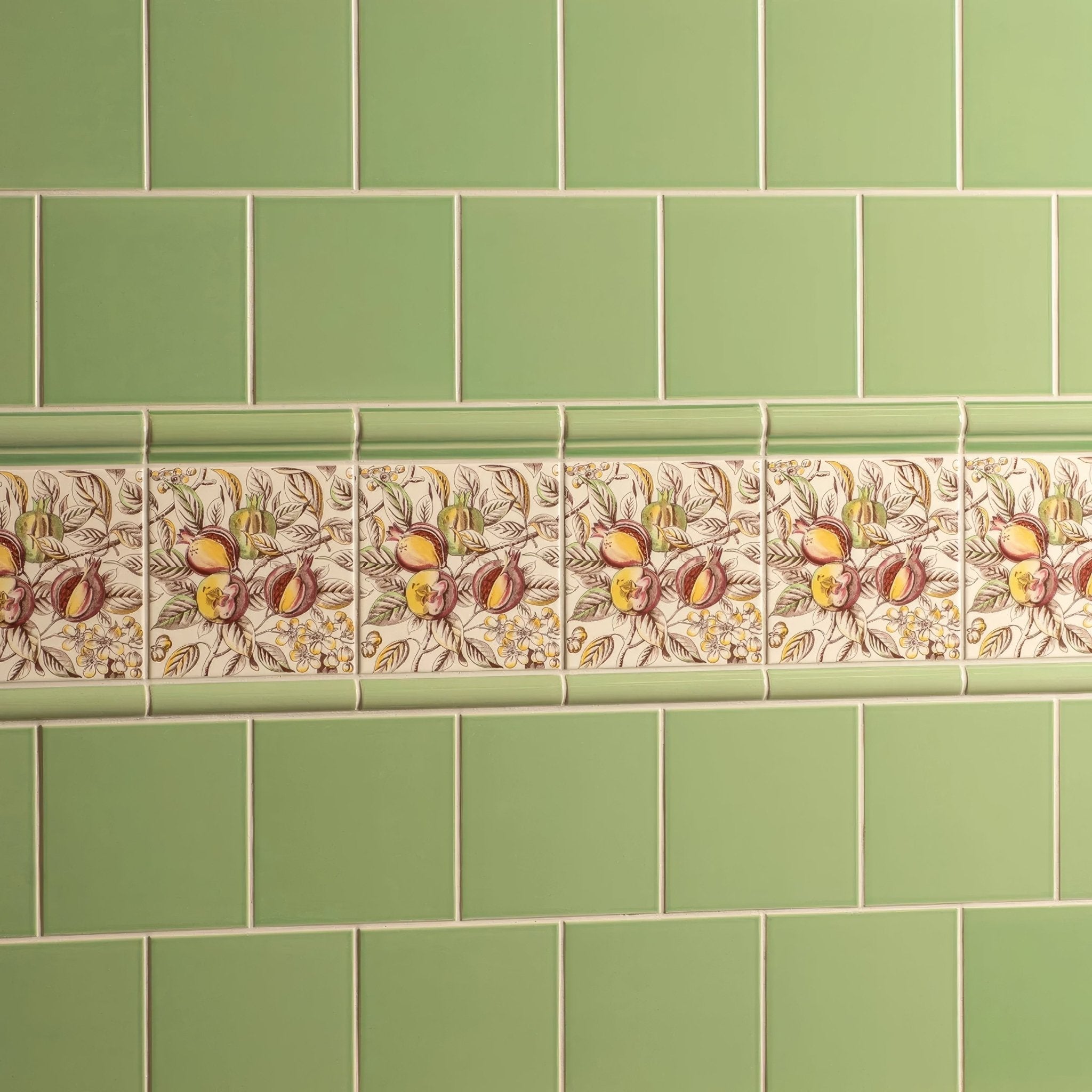A decorative ceramic tile border from artworks palm green collection with pomegranates and foliage on cream background
