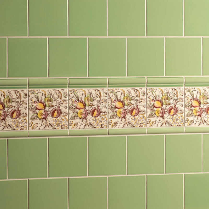 A decorative ceramic tile border from artworks palm green collection with pomegranates and foliage on cream background