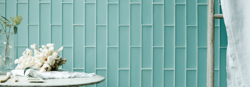 Aurora glass tiles in light teal feature a vertical rectangular design with subtle white grout lines on a tile wall