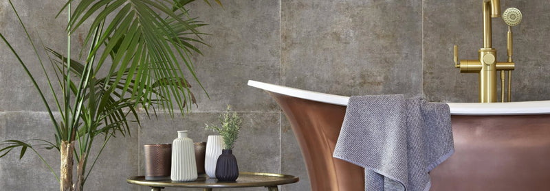 Copper-colored freestanding bathtub with gold-toned faucet and gray towel in bathroom wall tiles collection.