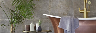 Copper-colored freestanding bathtub with gold-toned faucet and gray towel in bathroom wall tiles collection.
