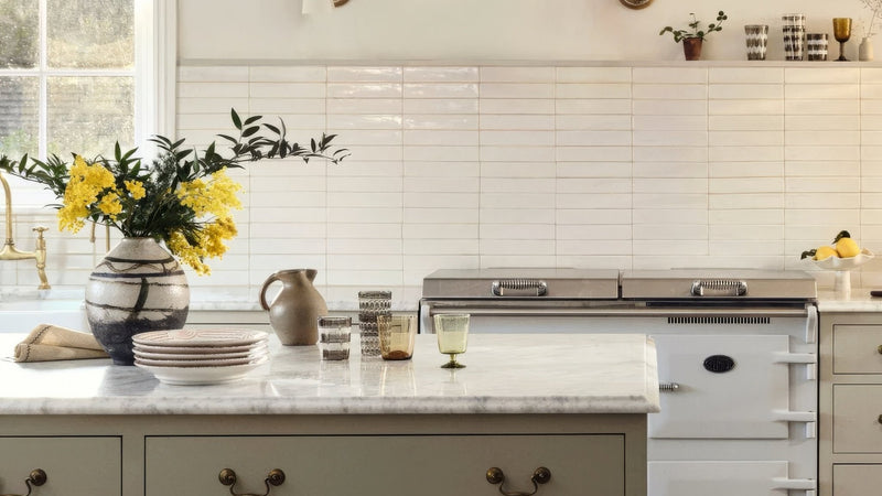A ceramic vase with black and white stripes holding bright yellow flowers in a beige wall tiles collection